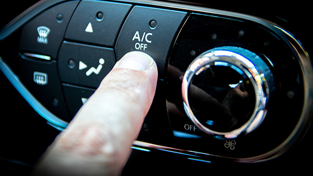 An image of a hand pressing the  A C  button on a car s dashboard, with the interior lighting illuminating the control panel.